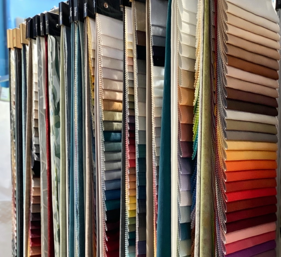 Mehrere Stoffmuster in unterschiedlichen Farben hängen an einem Musterständer.